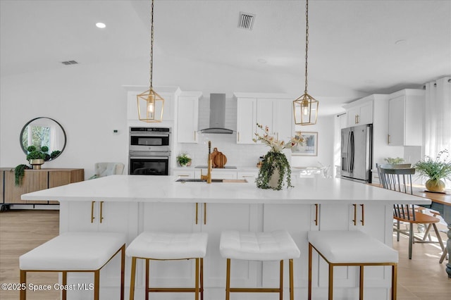 kitchen featuring appliances with stainless steel finishes, light countertops, decorative light fixtures, and wall chimney exhaust hood