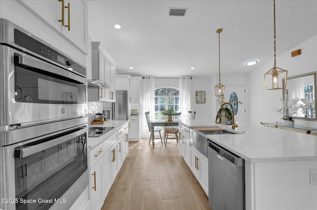 kitchen featuring stainless steel appliances, visible vents, white cabinets, an island with sink, and pendant lighting