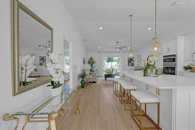 kitchen featuring hanging light fixtures, stainless steel double oven, open floor plan, white cabinets, and a kitchen bar