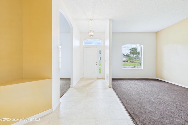 entrance foyer featuring arched walkways, a textured ceiling, carpet, and baseboards