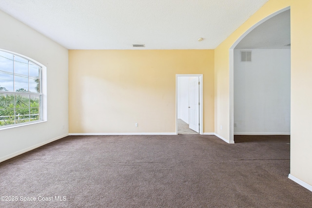 unfurnished room featuring arched walkways, dark carpet, visible vents, and baseboards