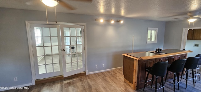 kitchen with a textured ceiling, baseboards, light wood-style flooring, and a ceiling fan