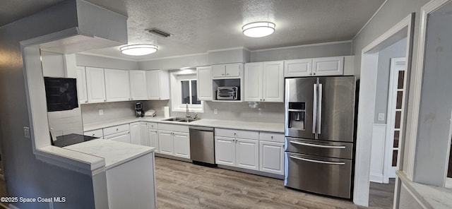 kitchen with light wood-type flooring, appliances with stainless steel finishes, white cabinets, and a sink