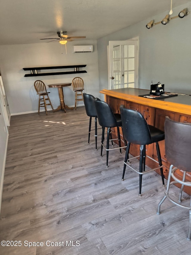 bar featuring a dry bar, baseboards, a ceiling fan, wood finished floors, and an AC wall unit