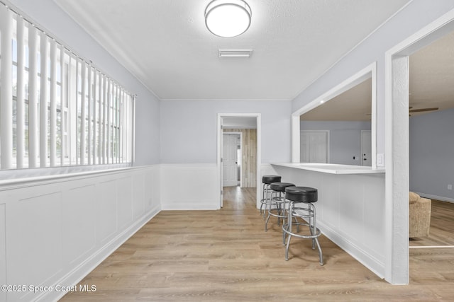 interior space featuring light wood finished floors, visible vents, a decorative wall, wainscoting, and a textured ceiling