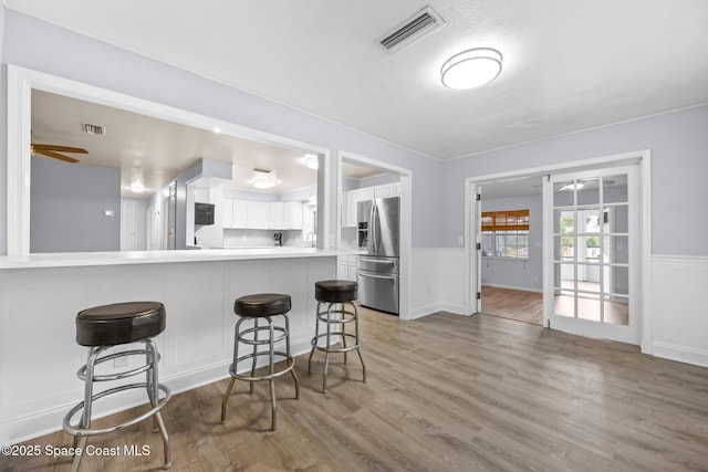 kitchen with white cabinets, visible vents, a wainscoted wall, and stainless steel fridge with ice dispenser