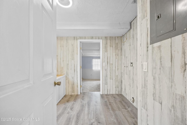 hallway with light wood-style floors, electric panel, and a textured ceiling