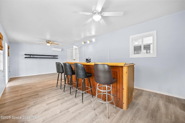 bar featuring baseboards, a ceiling fan, a bar, light wood-style floors, and a wall mounted AC