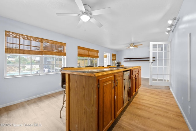 kitchen with a kitchen island, a ceiling fan, baseboards, light wood-style floors, and brown cabinetry