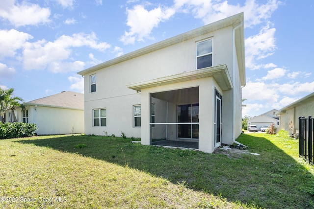 back of property with a sunroom, a lawn, and stucco siding