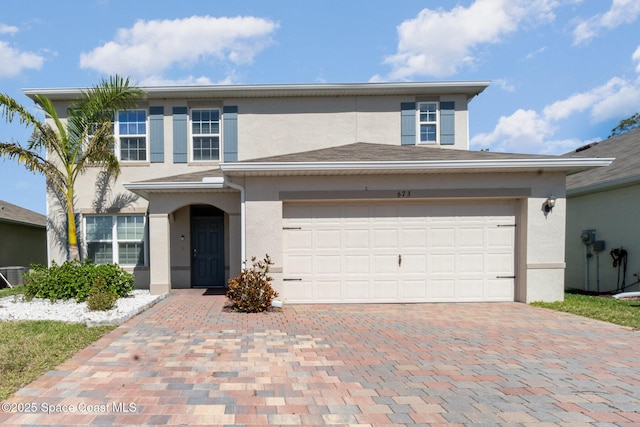 traditional-style home with a garage, decorative driveway, and stucco siding