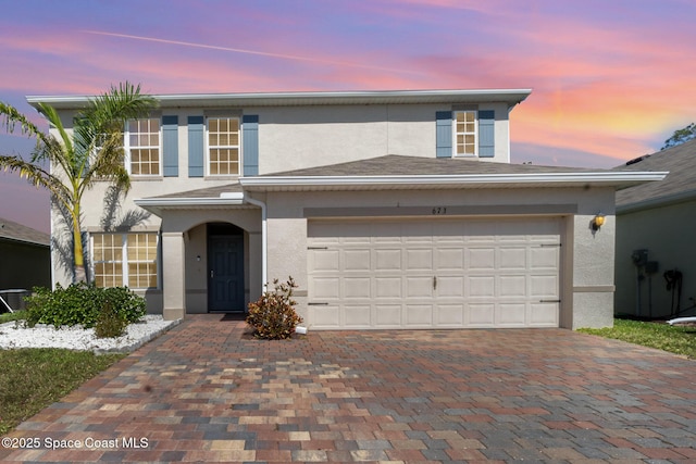 traditional-style house with a garage, decorative driveway, and stucco siding