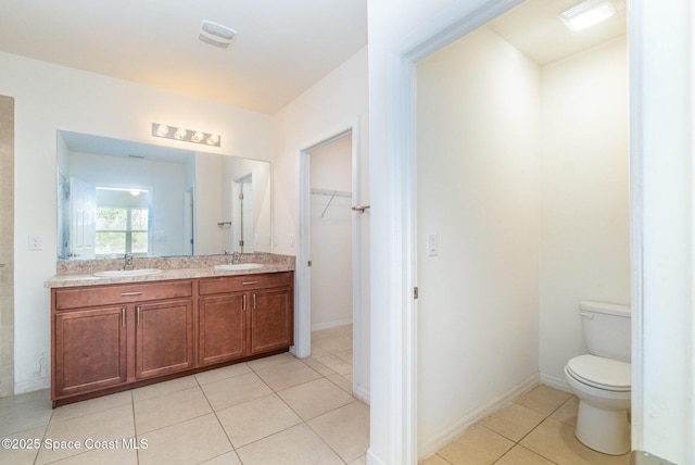 bathroom with toilet, a spacious closet, a sink, and tile patterned floors