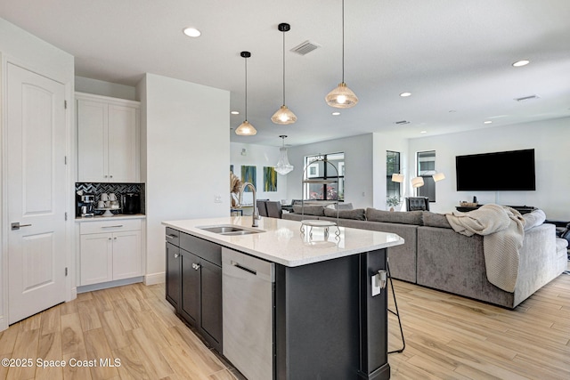 kitchen featuring light wood finished floors, visible vents, stainless steel dishwasher, white cabinets, and a sink