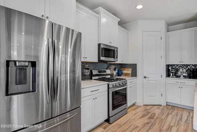 kitchen with stainless steel appliances, light wood-style flooring, white cabinetry, and decorative backsplash