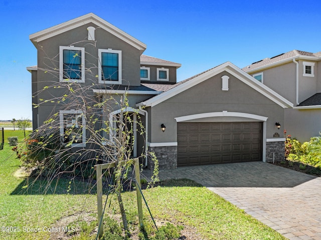 traditional-style house featuring an attached garage, stone siding, decorative driveway, stucco siding, and a front lawn