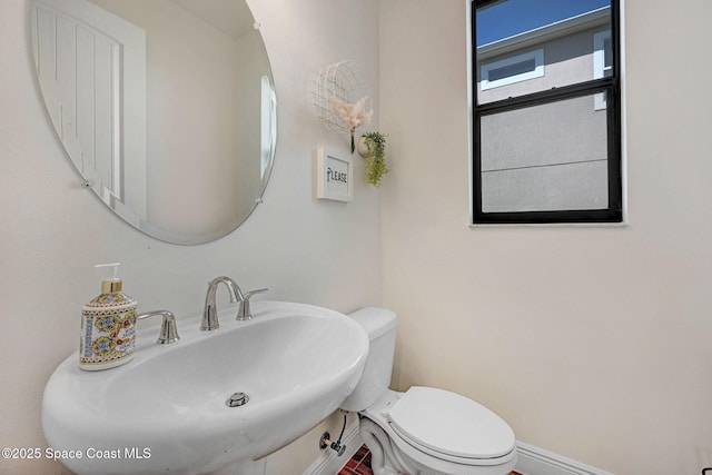 half bath with a sink, toilet, and baseboards