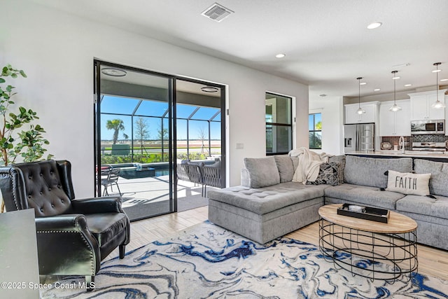 living area with a wealth of natural light, a sunroom, visible vents, and light wood-style flooring