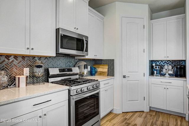 kitchen with light stone counters, light wood-style flooring, stainless steel appliances, white cabinetry, and backsplash