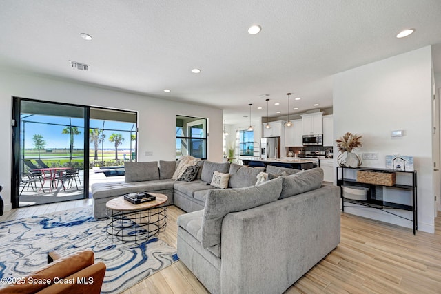 living room with recessed lighting, visible vents, a textured ceiling, and light wood finished floors