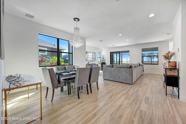 dining room with baseboards, light wood finished floors, a healthy amount of sunlight, and an inviting chandelier