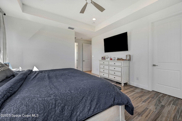 bedroom featuring a tray ceiling, visible vents, a ceiling fan, wood finished floors, and baseboards