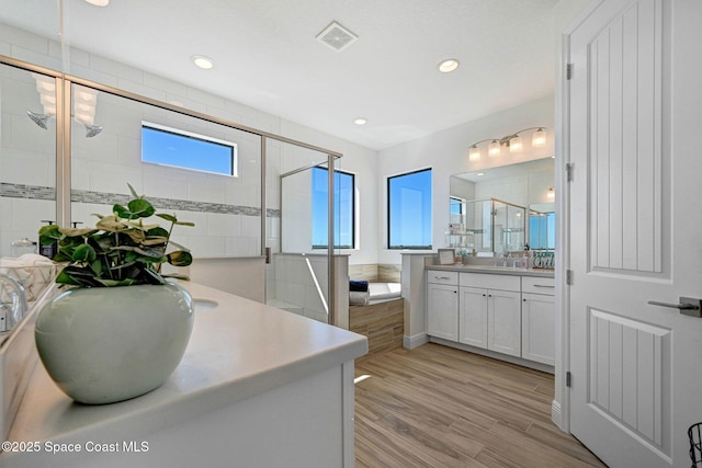 full bath featuring wood finished floors, two vanities, a shower stall, and a bath