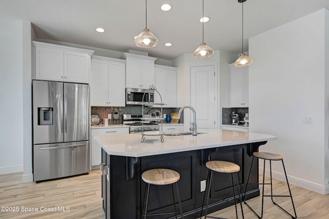 kitchen with decorative backsplash, appliances with stainless steel finishes, white cabinetry, a sink, and light wood-type flooring