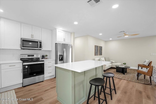 kitchen with stainless steel appliances, a kitchen bar, light countertops, and white cabinets