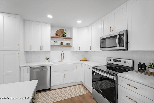 kitchen featuring stainless steel appliances, light countertops, white cabinetry, open shelves, and a sink