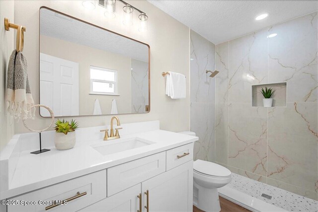 full bath featuring a marble finish shower, toilet, vanity, and a textured ceiling