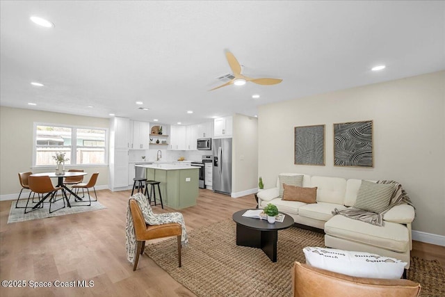 living area featuring baseboards, a ceiling fan, light wood-style flooring, and recessed lighting