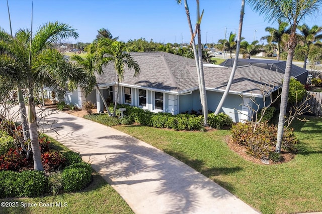 view of front of property with roof with shingles, a front lawn, concrete driveway, and stucco siding