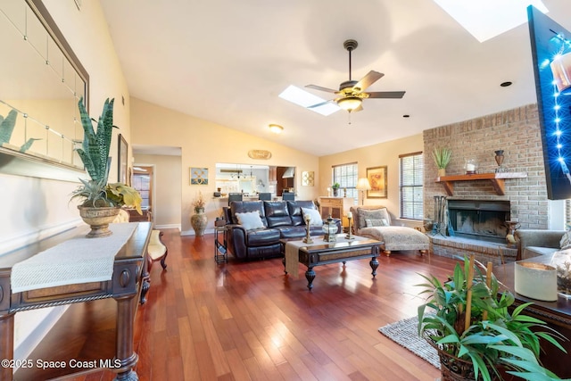 living room with a skylight, ceiling fan, wood finished floors, a fireplace, and high vaulted ceiling