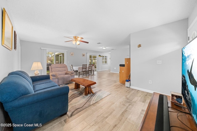 living area featuring light wood-type flooring, baseboards, and a ceiling fan