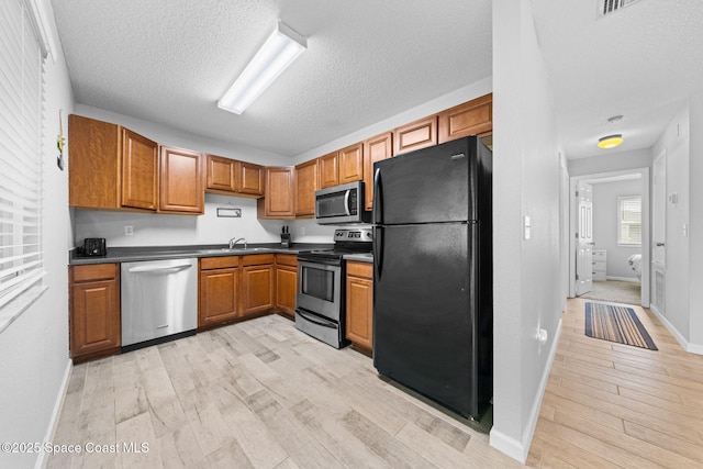 kitchen featuring dark countertops, light wood-type flooring, brown cabinets, and stainless steel appliances