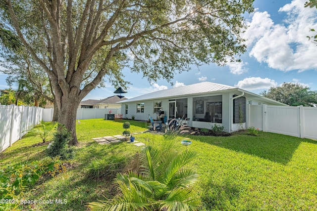 back of house with a sunroom, a fenced backyard, metal roof, and a yard