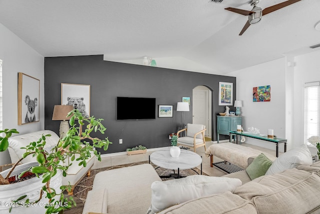 living room with lofted ceiling, tile patterned flooring, arched walkways, and a ceiling fan