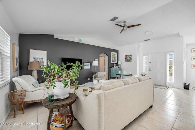 living room featuring arched walkways, light tile patterned floors, lofted ceiling, visible vents, and ceiling fan