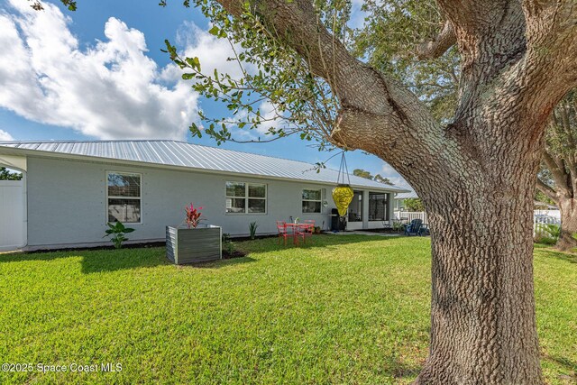 rear view of property with metal roof, a lawn, and stucco siding