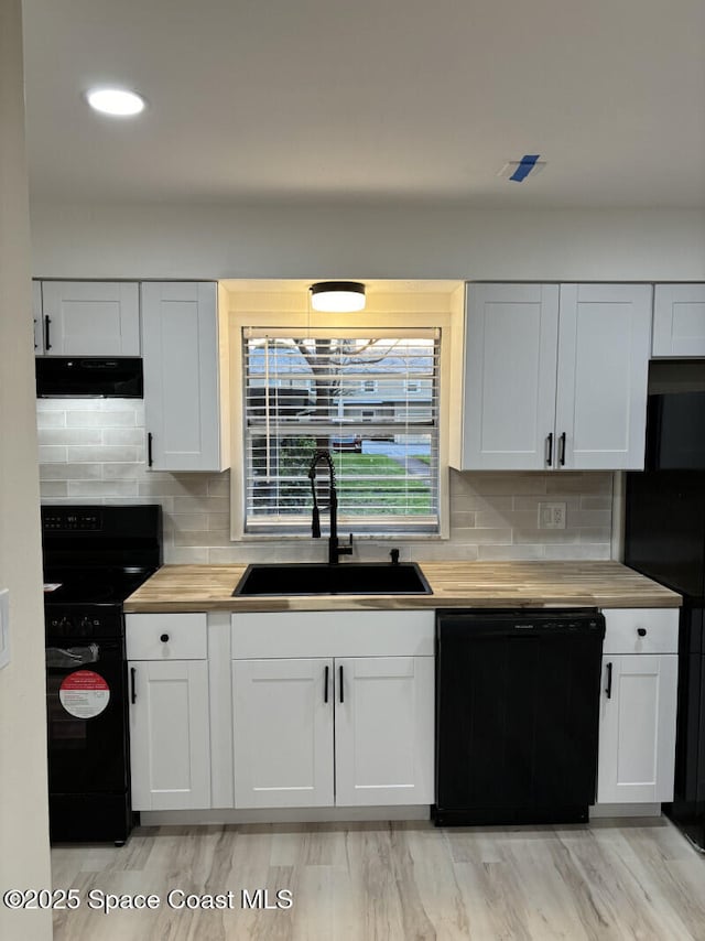 kitchen featuring butcher block counters, extractor fan, black appliances, white cabinetry, and a sink