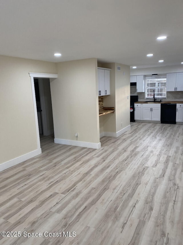 unfurnished living room with recessed lighting, baseboards, a sink, and light wood finished floors