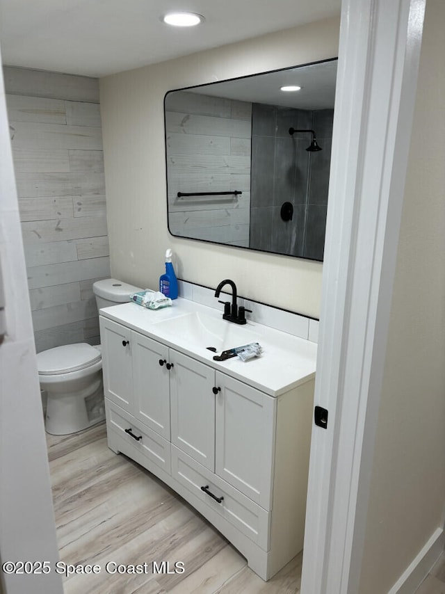 full bathroom with toilet, tiled shower, wood finished floors, and vanity