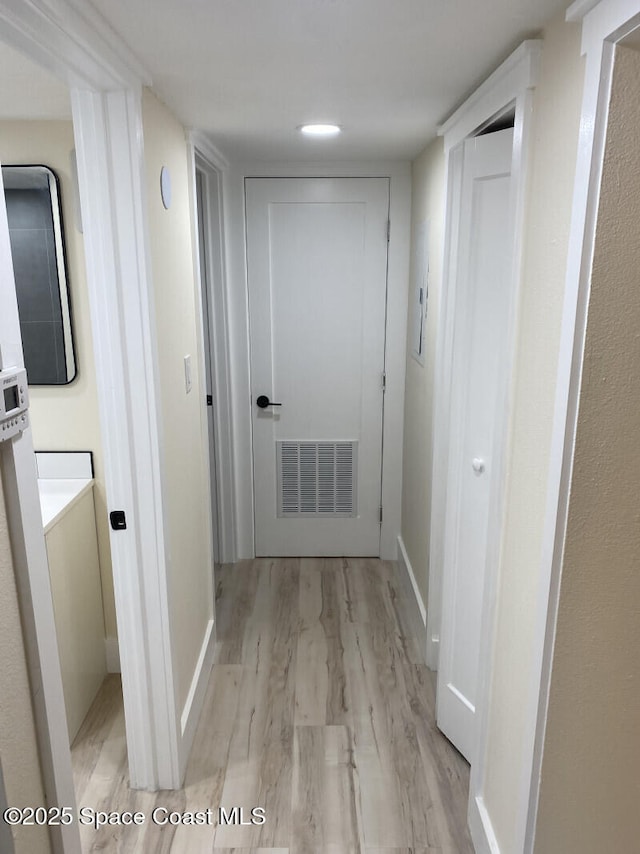 hall with light wood-type flooring, visible vents, and baseboards