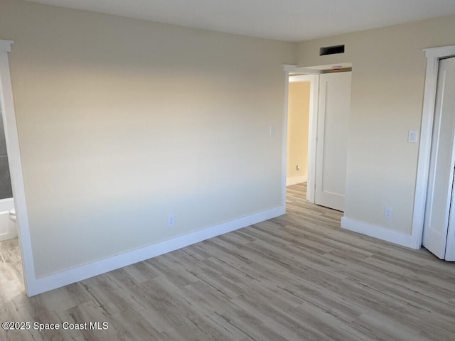 unfurnished bedroom featuring ensuite bath, light wood finished floors, visible vents, and baseboards