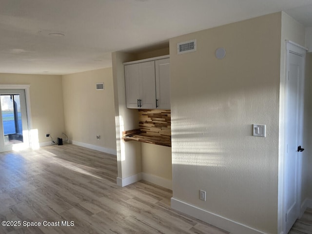 kitchen featuring light wood finished floors, tasteful backsplash, visible vents, white cabinets, and baseboards