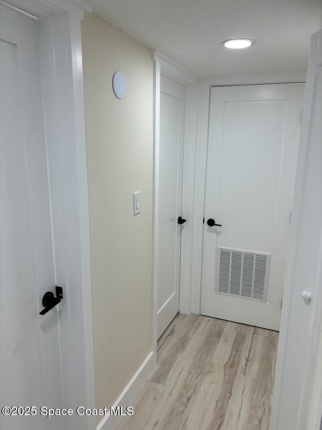 hall featuring light wood-type flooring, visible vents, and baseboards