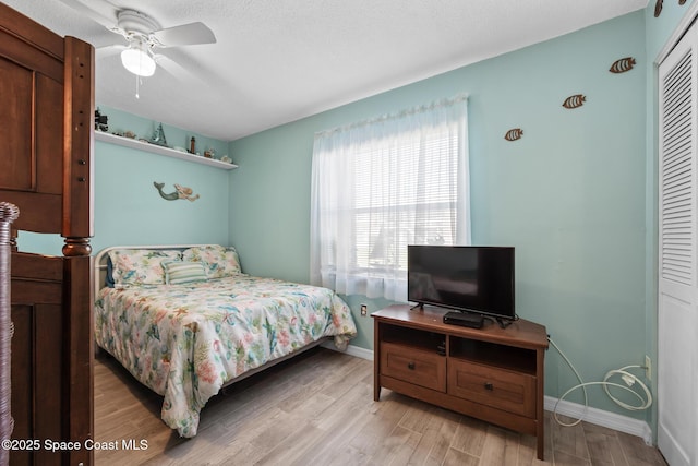 bedroom featuring light wood finished floors, a closet, ceiling fan, a textured ceiling, and baseboards