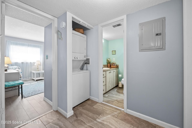 laundry room with stacked washer and dryer, visible vents, a textured ceiling, laundry area, and electric panel