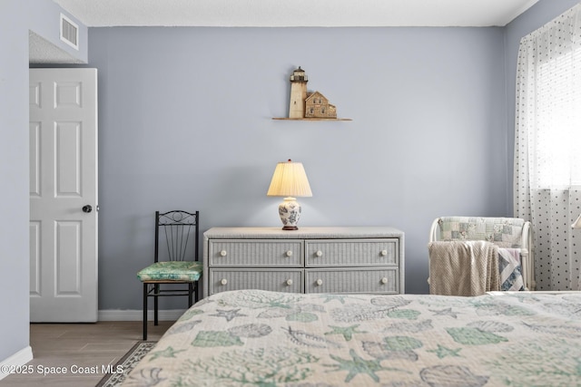 bedroom with baseboards, visible vents, and wood finished floors